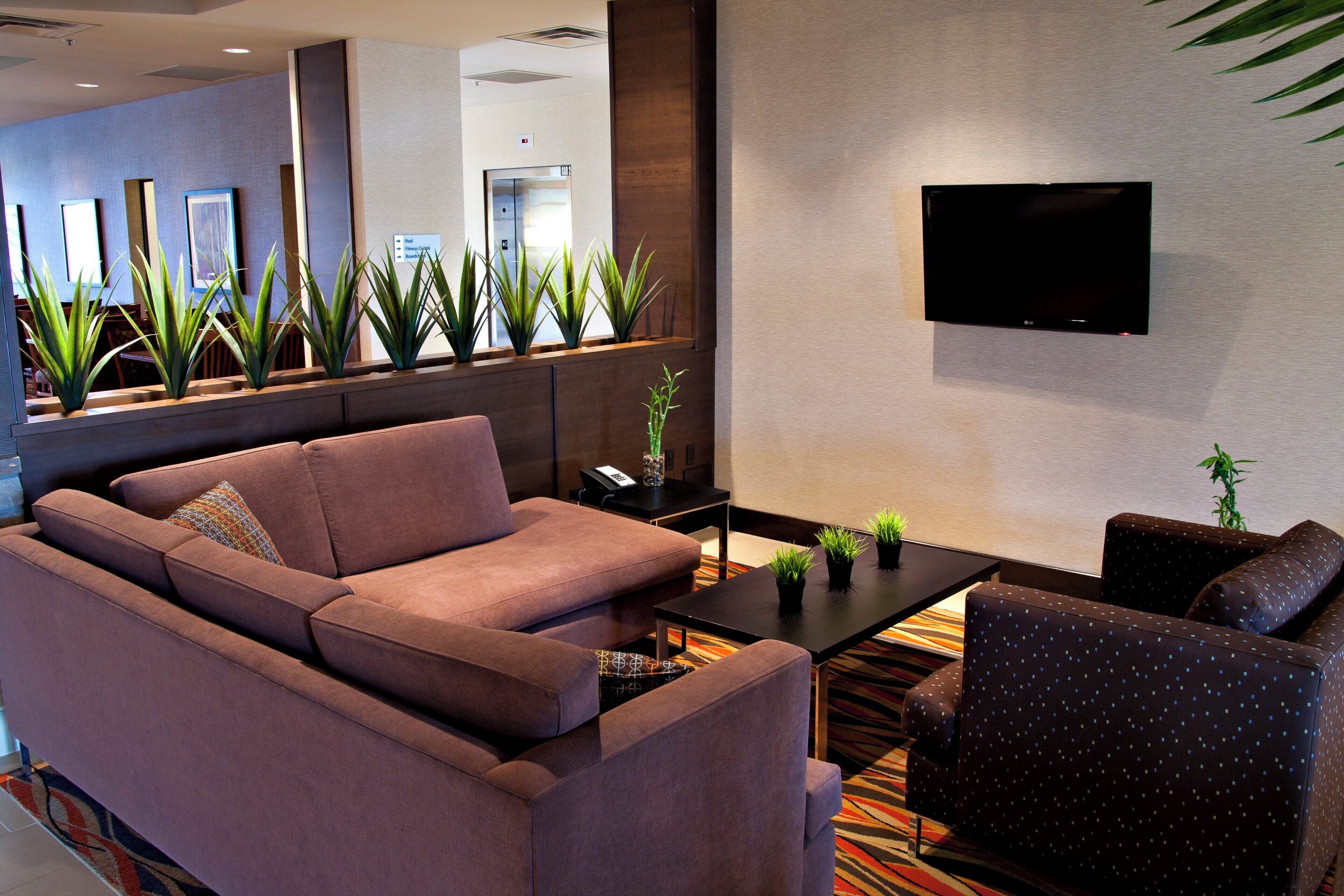 Um saguão de hotel moderno com um sofá, poltronas, uma mesa de centro e uma TV de tela plana na parede.