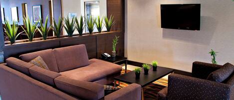 Um saguão de hotel moderno com um sofá, poltronas, uma mesa de centro e uma TV de tela plana na parede.