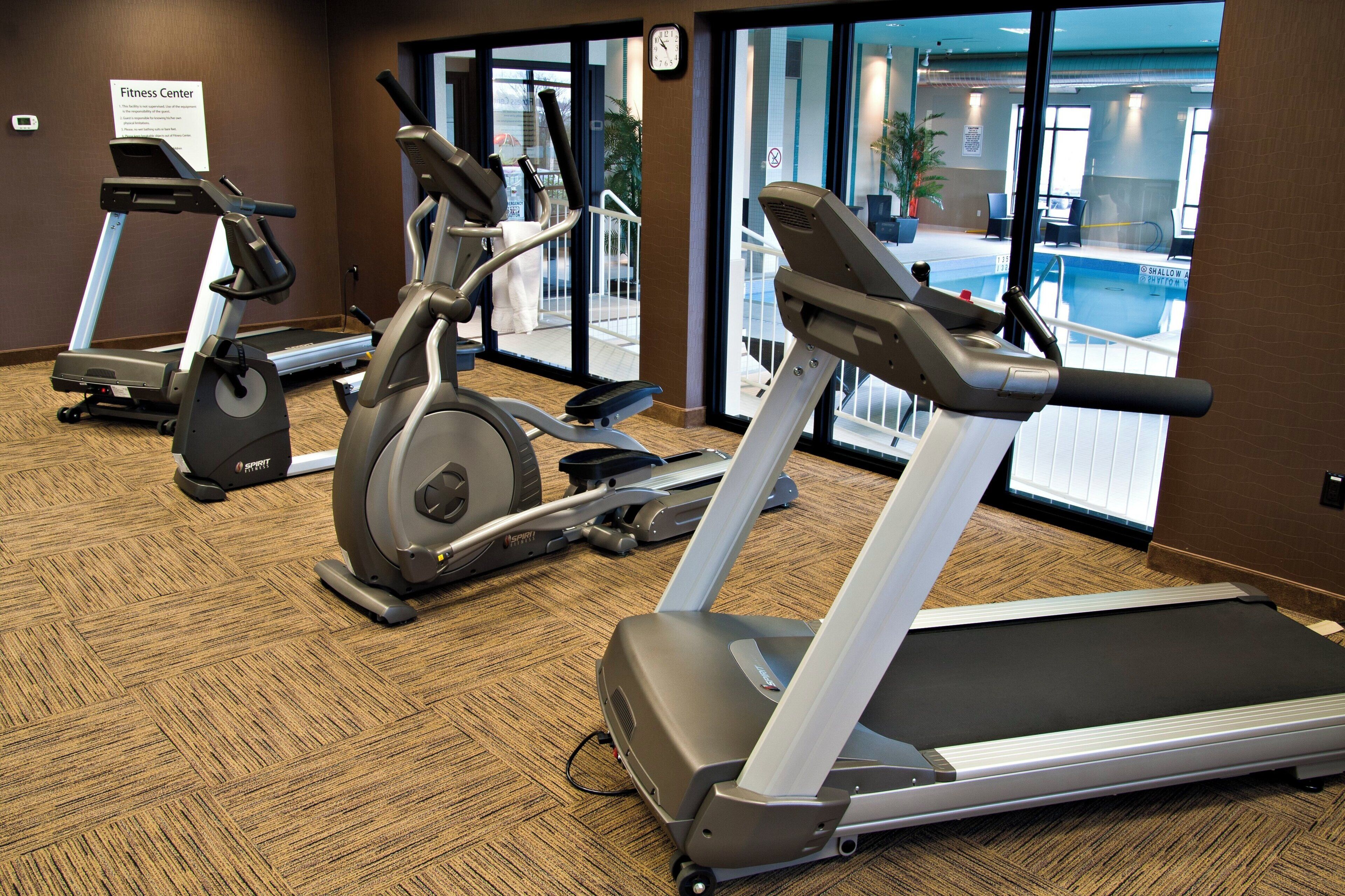 Et fitnesscenter med løbebånd, motionscykler og udsigt til en pool.