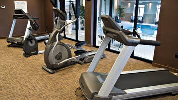 Et fitnesscenter med løbebånd, motionscykler og udsigt til en pool.