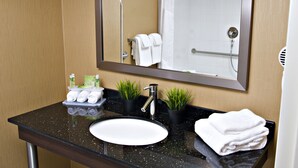 A bathroom with a black countertop, white sink, and a mirror above it. There are towels and toiletries on the counter. - Holiday Inn Express Pembroke by IHG (Pembroke)