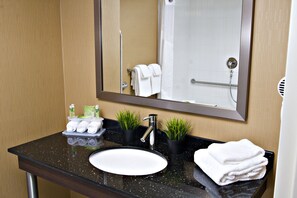 A bathroom with a black countertop, white sink, and a mirror above it. There are towels and toiletries on the counter. - Holiday Inn Express Pembroke by IHG (Pembroke)