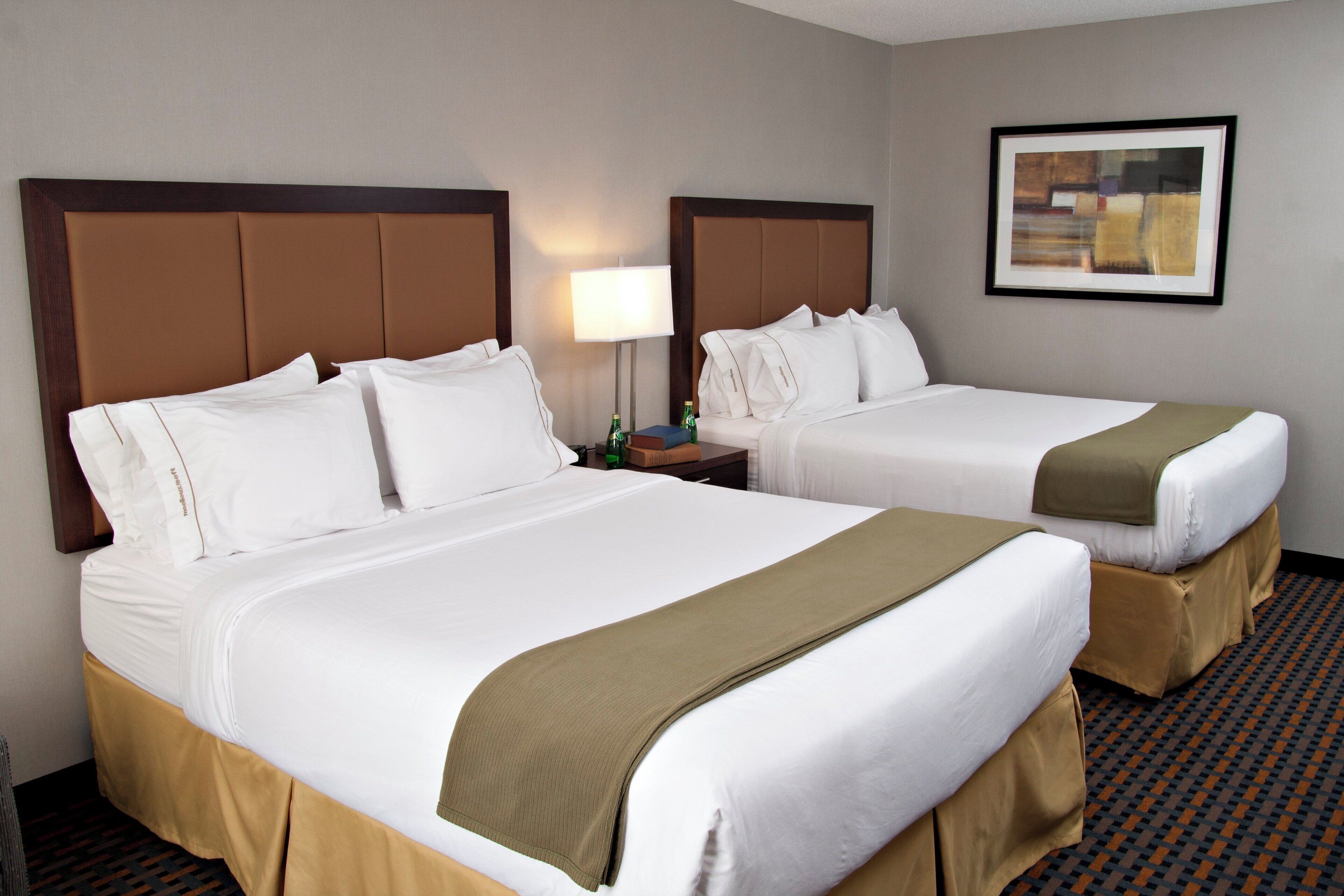 A hotel room with two beds, a nightstand, a lamp, and a framed picture on the wall.