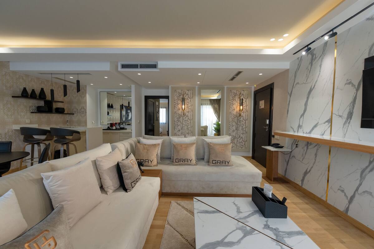 A modern living room with a sofa set, a marble coffee table, and a kitchen area visible in the background.