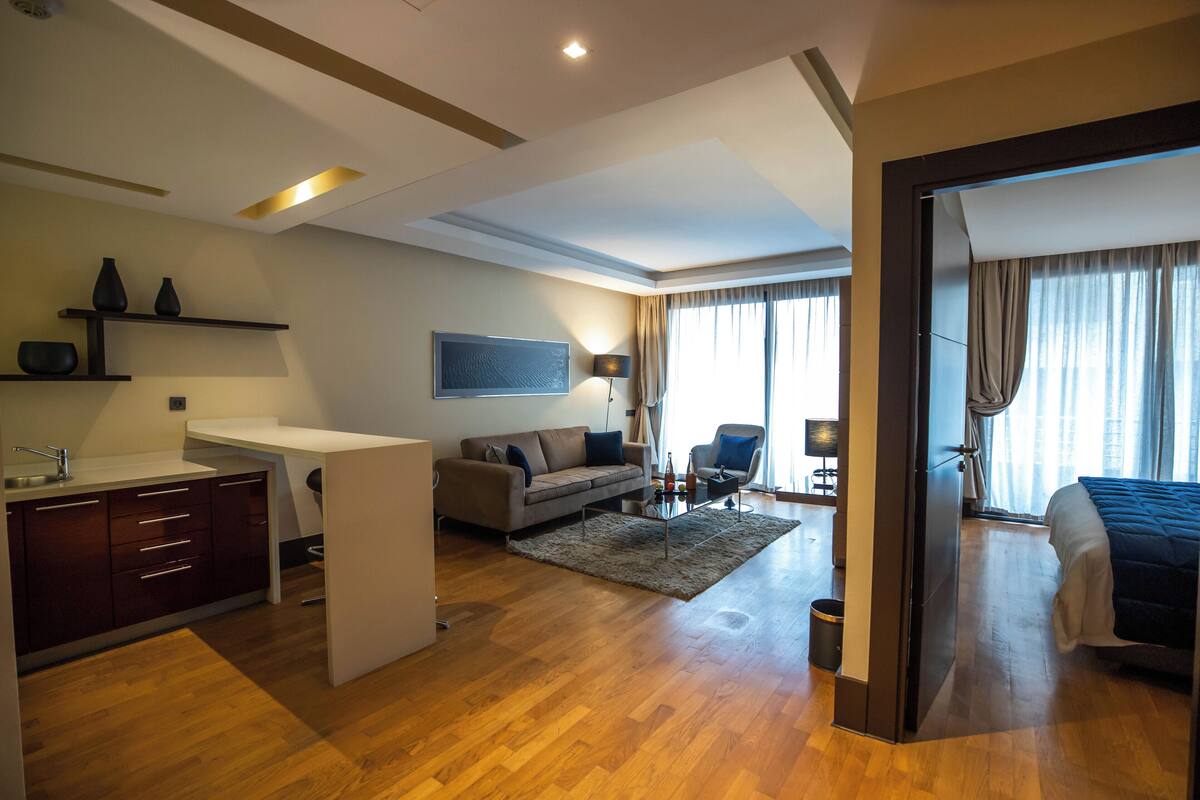 A modern hotel room with a wooden floor, a sofa, a desk, a bed, and a TV.