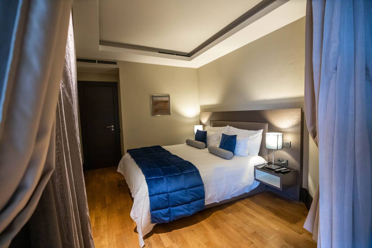 A hotel room with a large bed, a bedside table with a lamp, and a door.