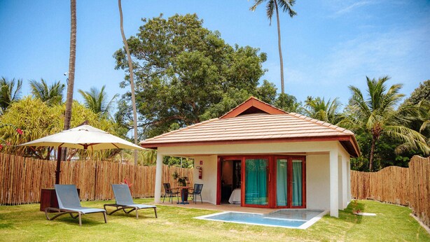 A small house with a red roof, a glass door, and a patio with two lounge chairs and a table.