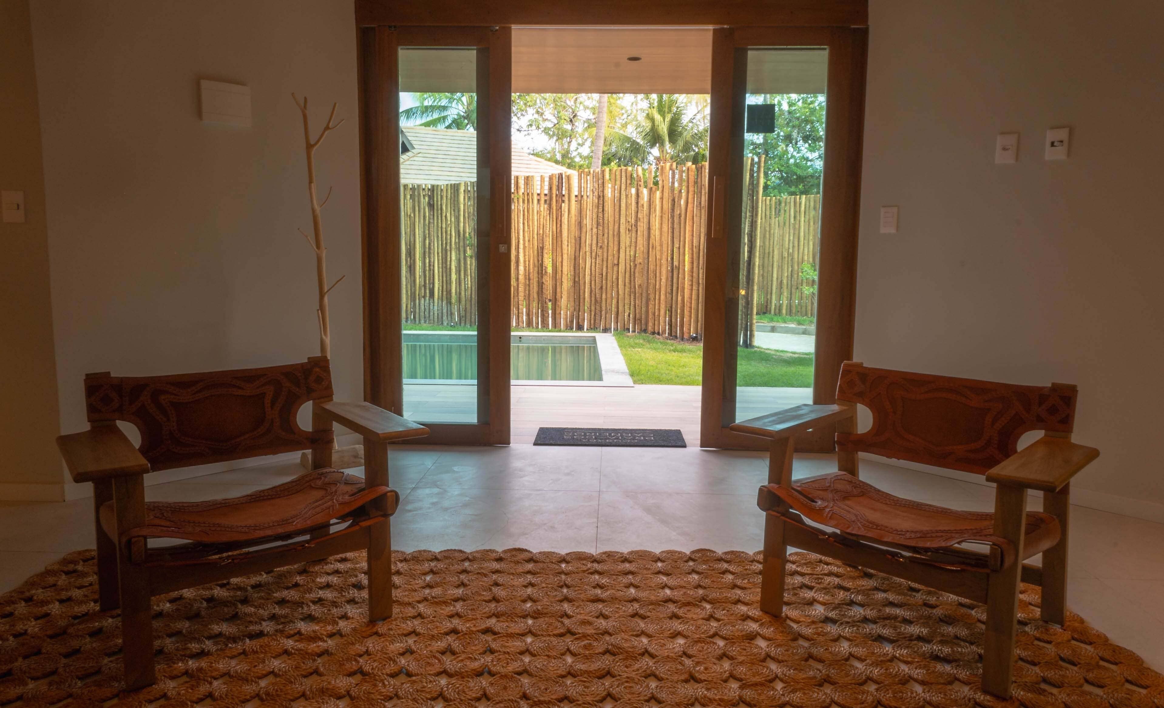 Una habitación con dos sillas de madera orientadas hacia una puerta corrediza de vidrio que da a un patio trasero con piscina y valla de madera.