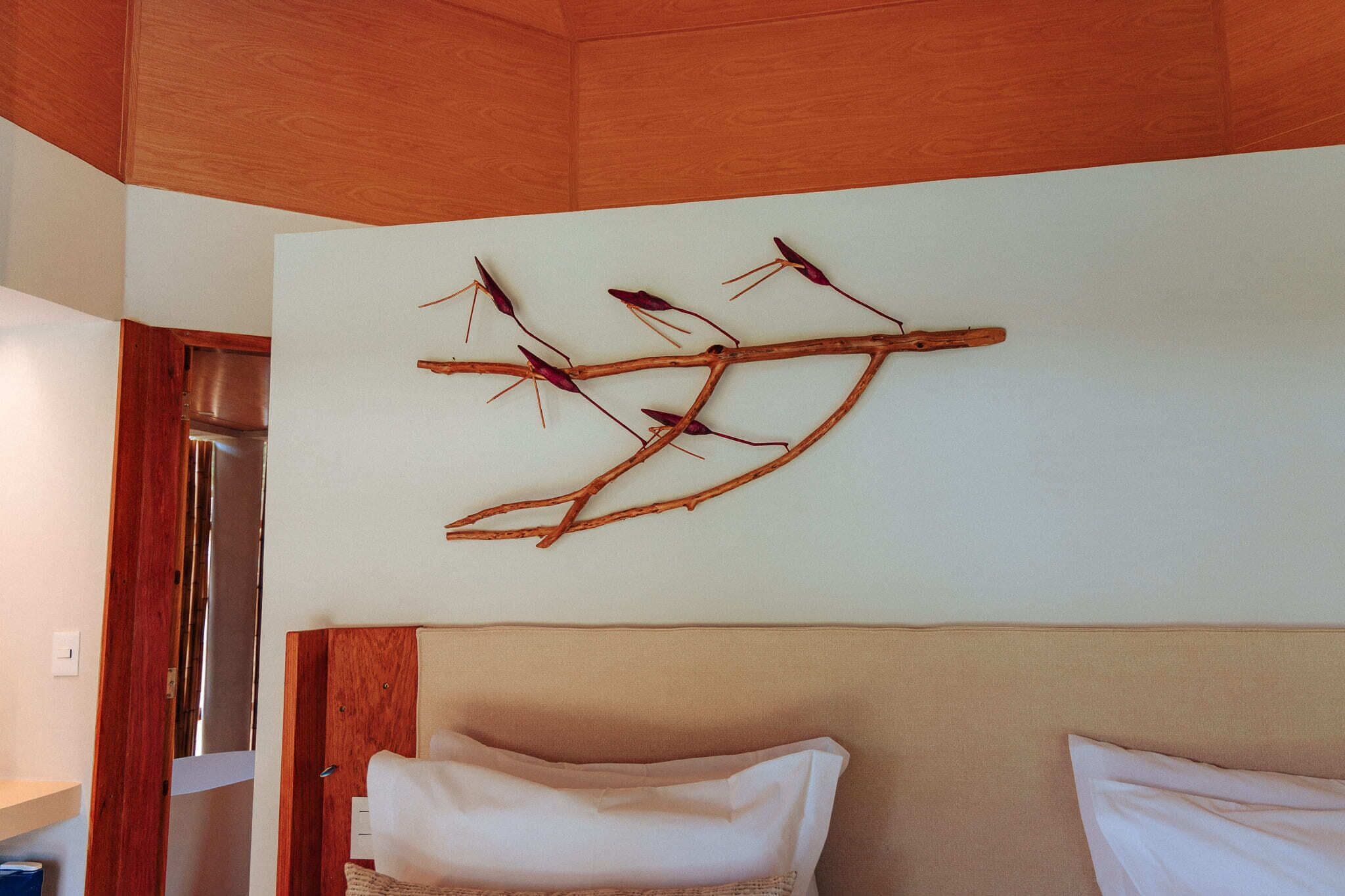 Un dormitorio con techo de madera, cama con ropa de cama blanca y una rama decorativa colgada en la pared.