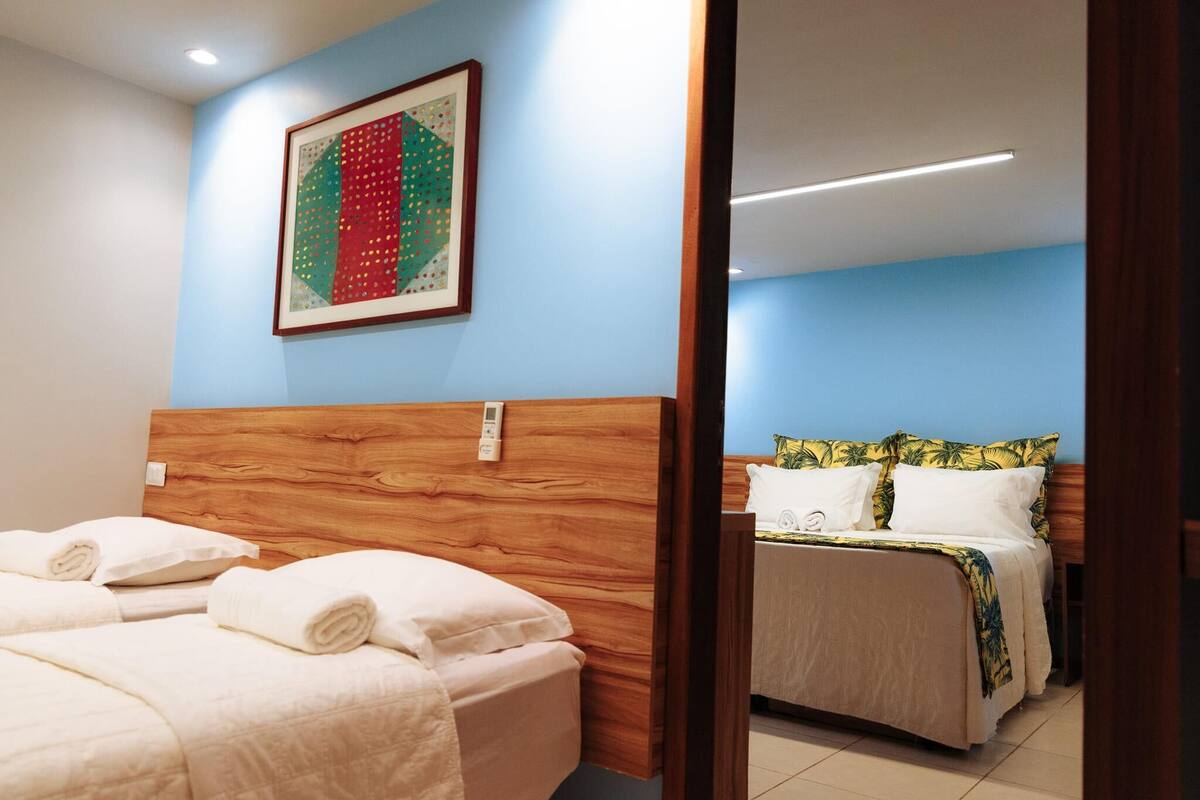 Habitación de hotel con dos camas, cabecero de madera, una obra de arte enmarcada en la pared y una mesita de noche con lámpara.