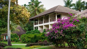 A two-story building with a balcony, surrounded by lush greenery and flowering plants.
