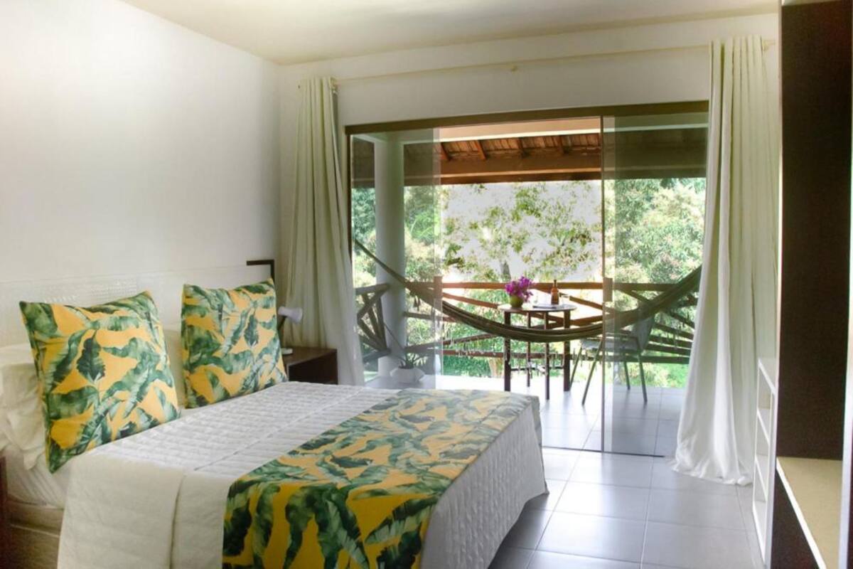 Un dormitorio con cama, mesita de noche, ventana con cortinas y vistas a un balcón con mesa y sillas.