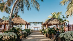A wooden pathway leading to a thatched-roof structure with white flowers on either side. - Pousada Praia dos Carneiros (Tamandaré)