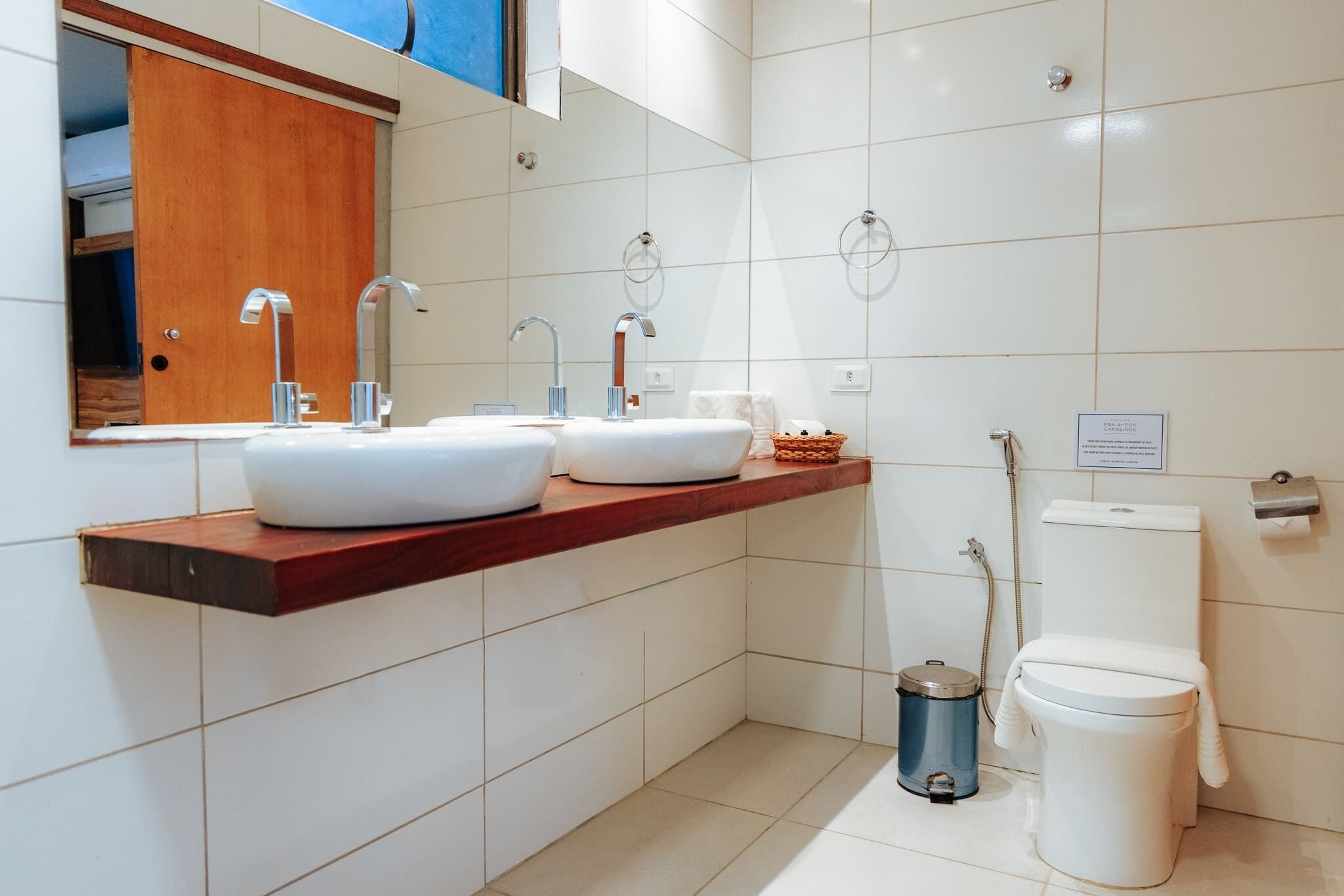 A modern bathroom with two sinks, a toilet, and a trash can.