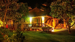 A wooden cabin with a porch, surrounded by trees and illuminated by warm lights. - Pousada Praia dos Carneiros (Tamandaré)