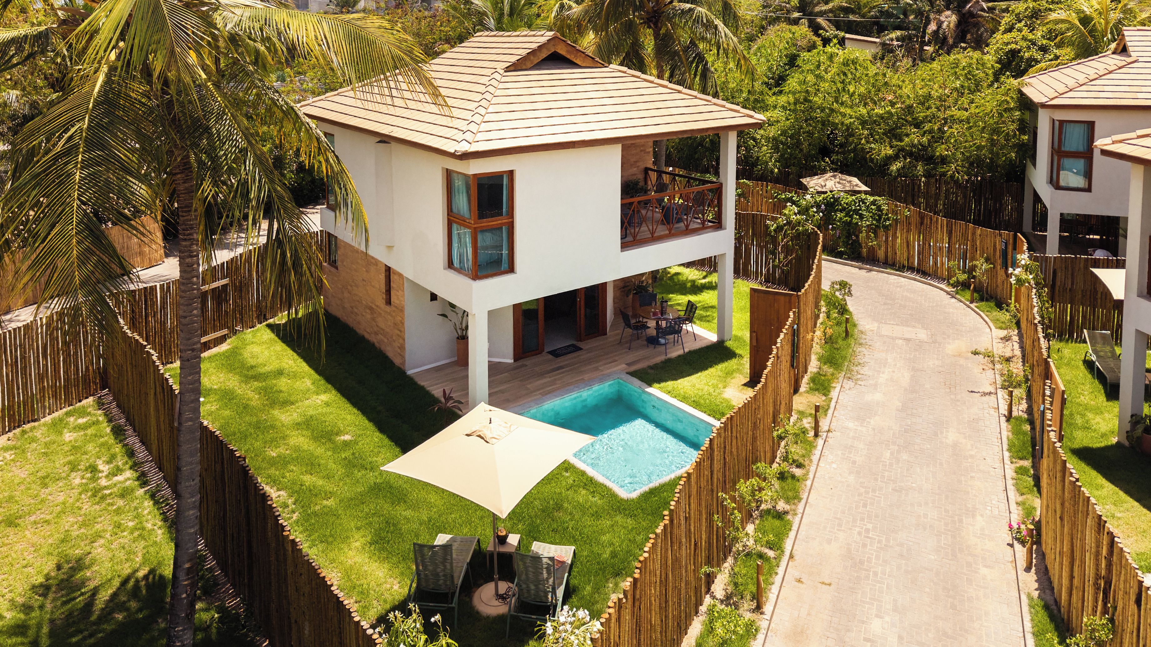 A two-story house with a swimming pool, surrounded by a wooden fence and lush greenery.