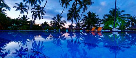 A pool reflecting palm trees and a sunset sky.