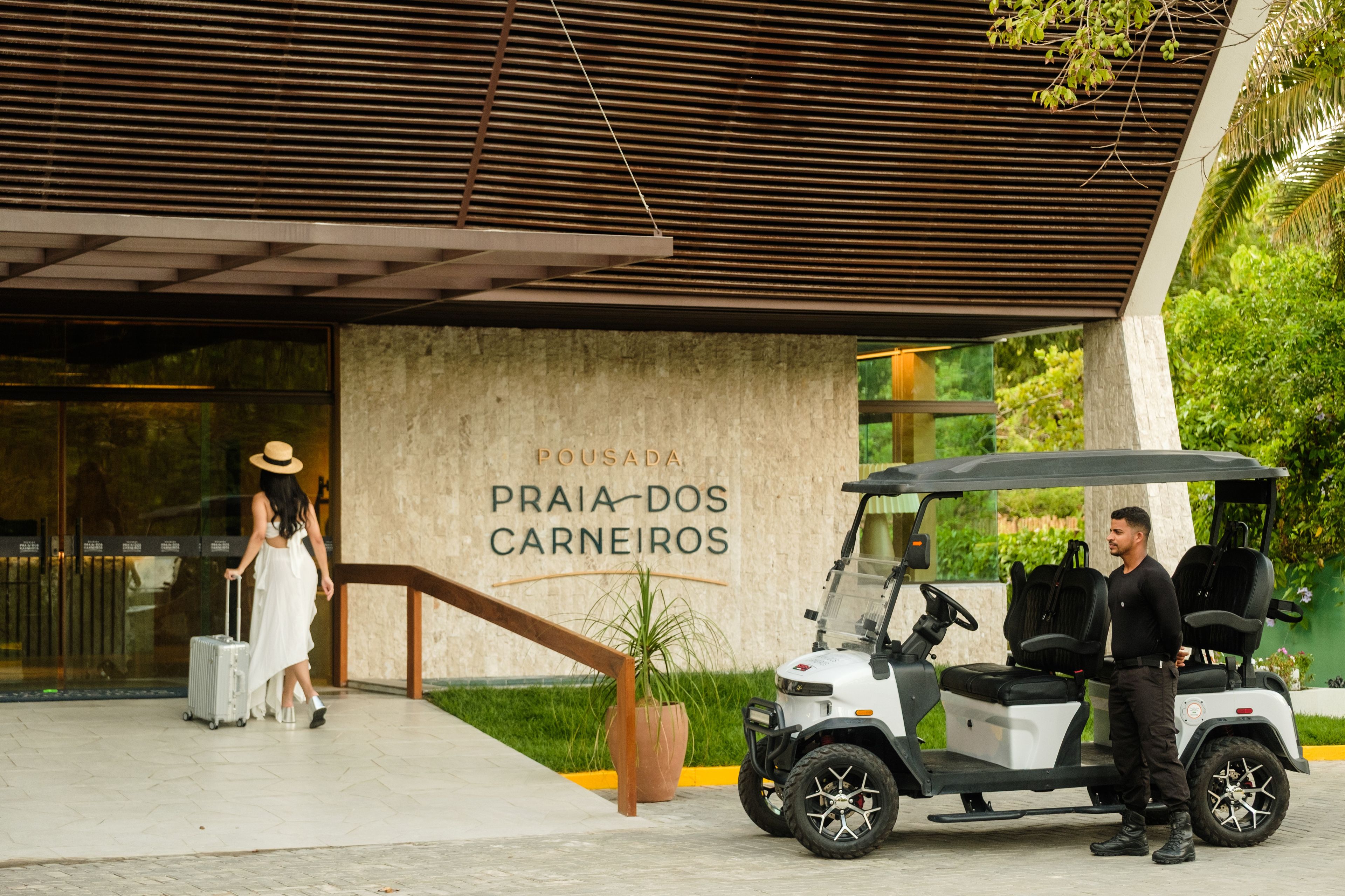 Carrinho de golfe estacionado em frente a um prédio com uma placa que diz 'Pousada Praia dos Carneiros'.