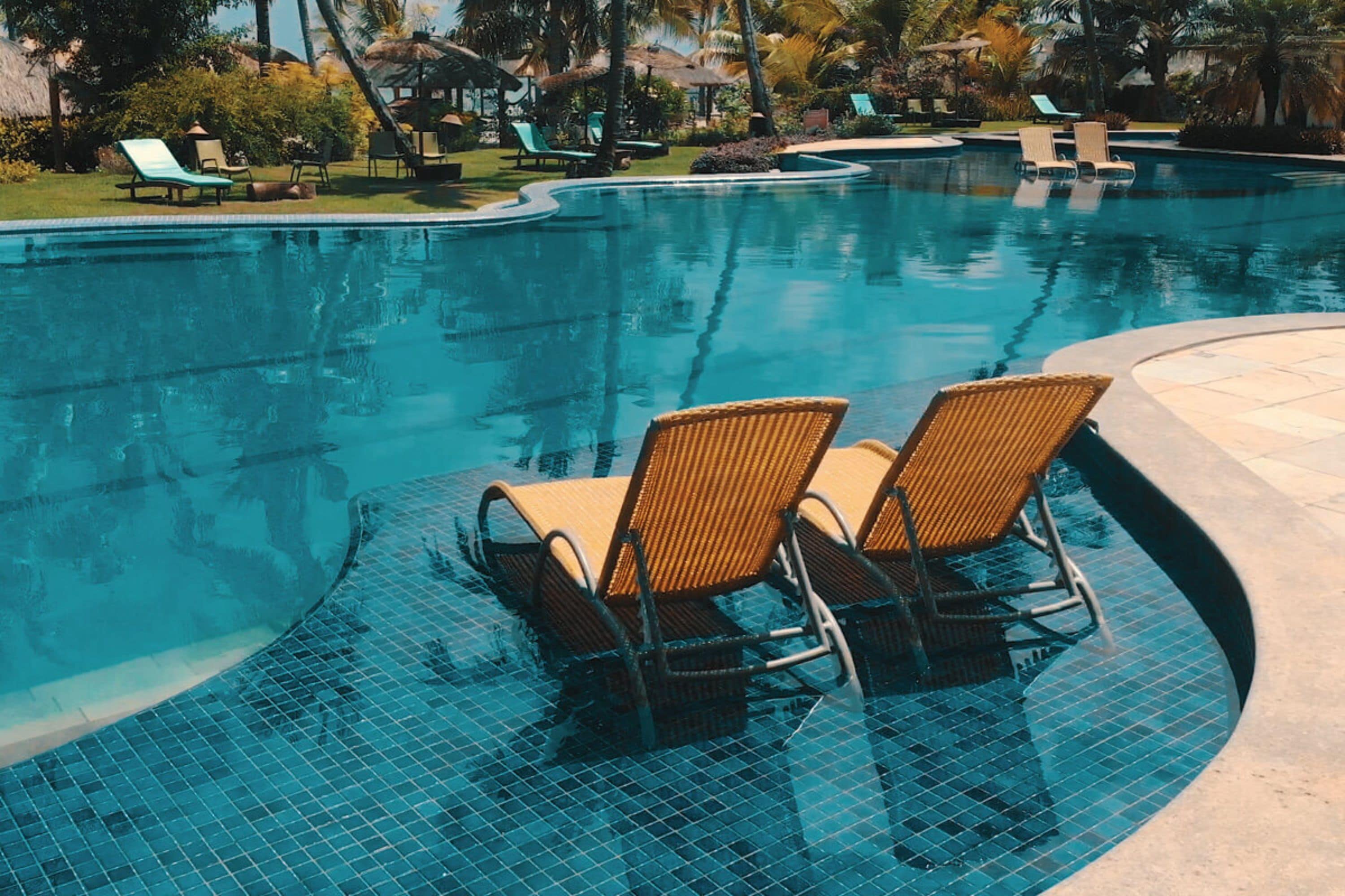 Une piscine avec deux chaises longues en osier et une terrasse carrelée.