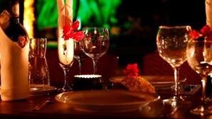 A dimly lit dining area with a table set for a meal, featuring wine glasses, a bottle, and a candle.