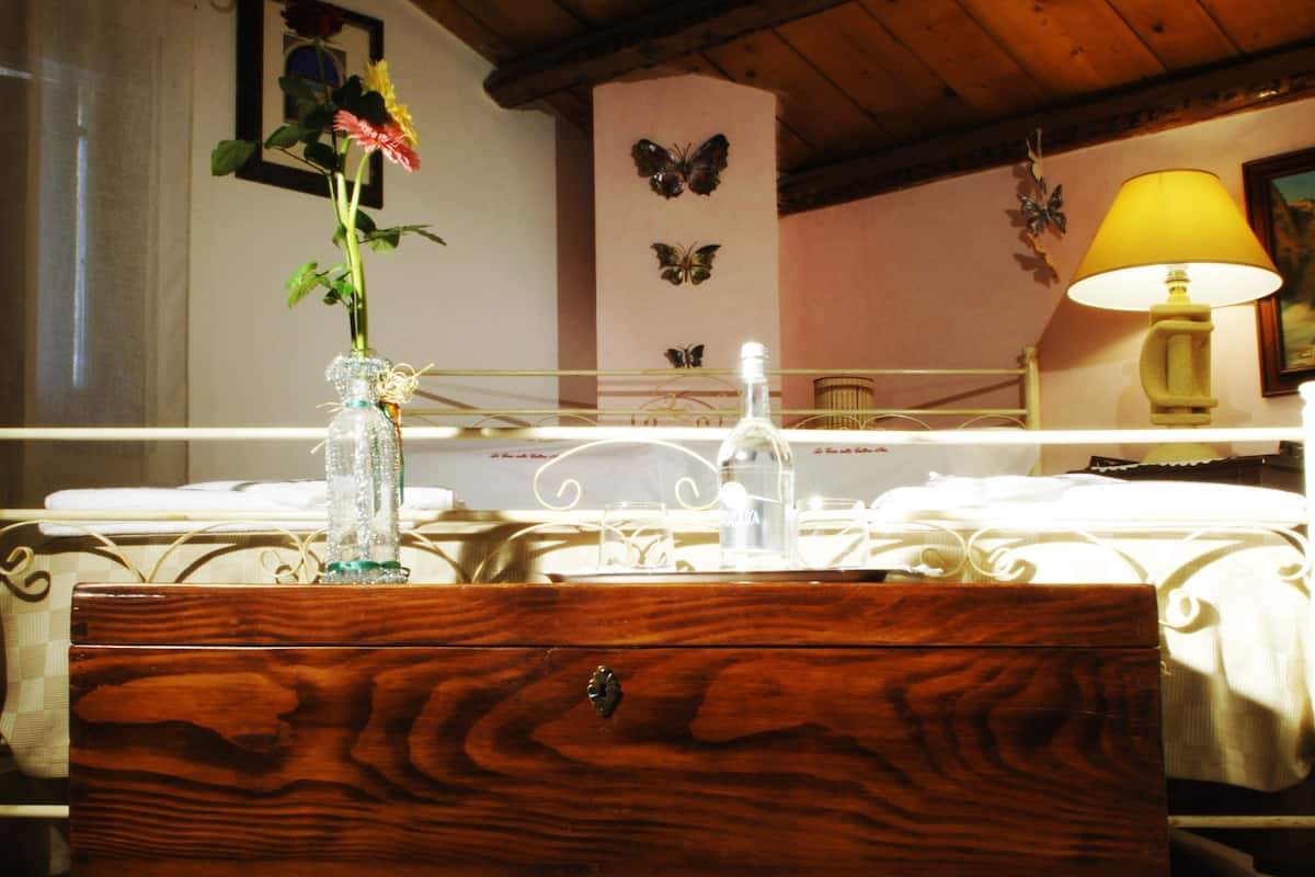 Une commode en bois, un vase en verre avec des fleurs, une table de chevet avec une lampe et un lit recouvert d’une couverture blanche.