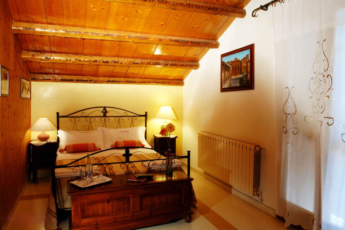Une chambre confortable avec un plafond en bois, un lit avec deux tables de chevet, un radiateur et un tableau encadré au mur.