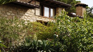 Una casa de piedra con balcón de madera, rodeada de abundante vegetación.
