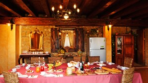 Comedor con una larga mesa dispuesta para una comida, rodeada de sillas de mimbre, un candelabro y una pared de piedra con un espejo.
