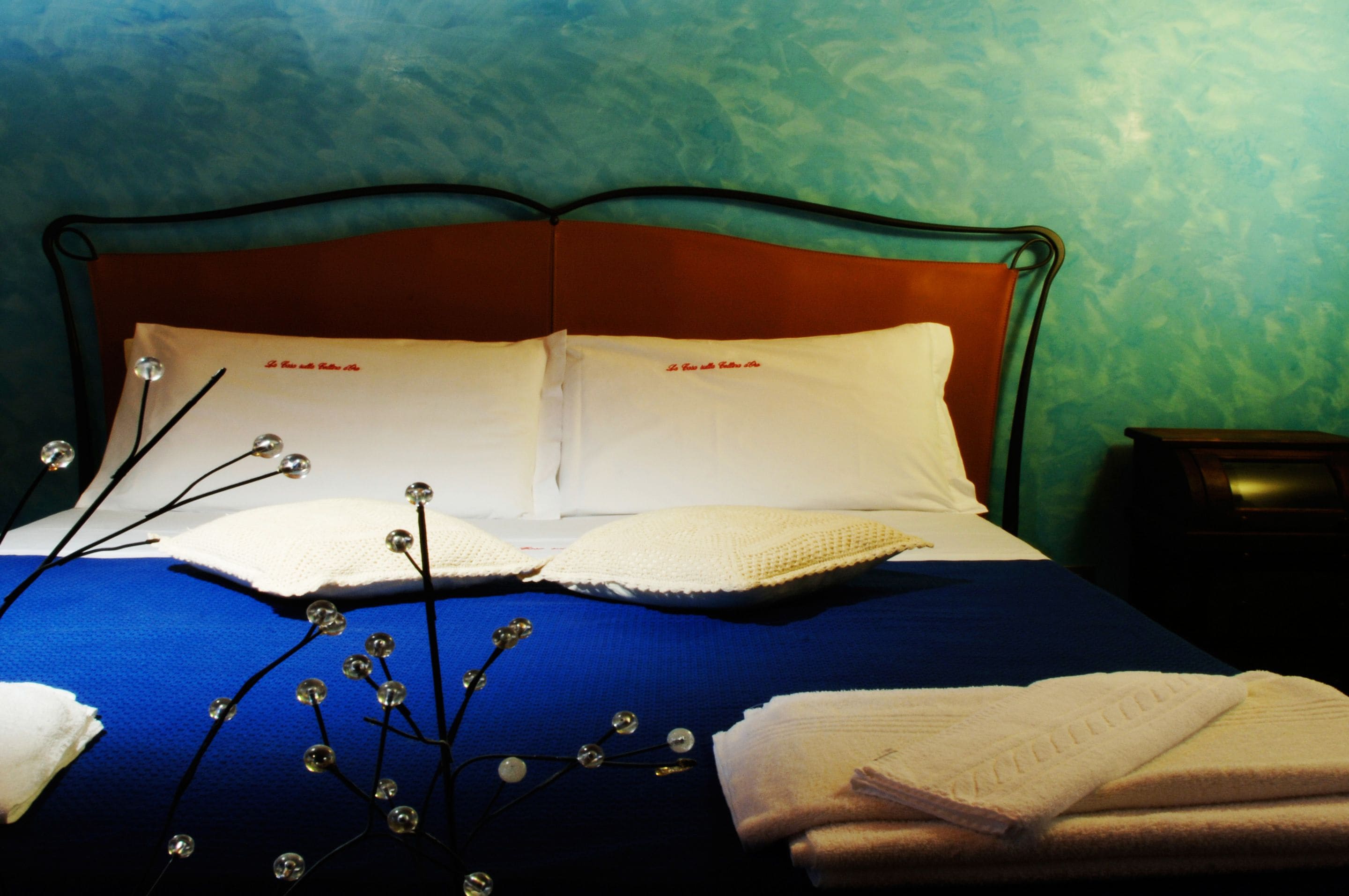 A neatly made bed with white linens, a blue blanket, and decorative elements like a white pillow and a branch with beads.