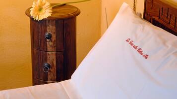 Uma cama com travesseiro branco e uma mesa de cabeceira de madeira com uma flor.