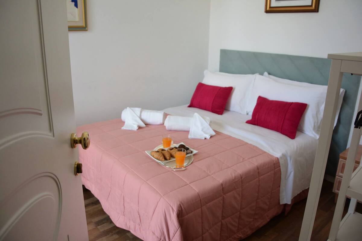 Une chambre d’hôtel avec un lit, des oreillers, une couvre-lit rose et un plateau avec de la nourriture et des boissons.