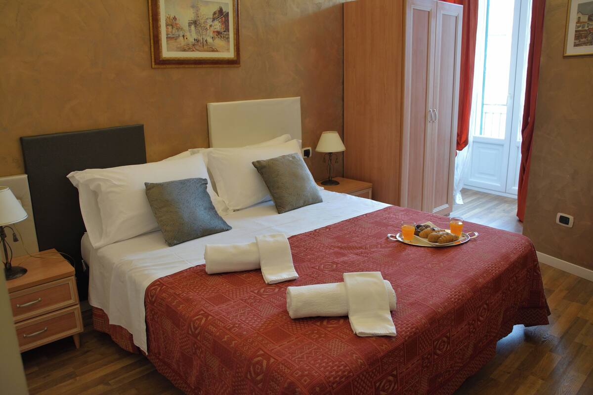 Une chambre d’hôtel avec un grand lit, une table de chevet avec une lampe, un plateau avec des articles pour le petit-déjeuner et un tableau au mur.