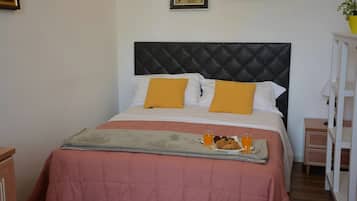 A neatly made bed with a quilted headboard, two pillows, and a tray with a drink and pastries.