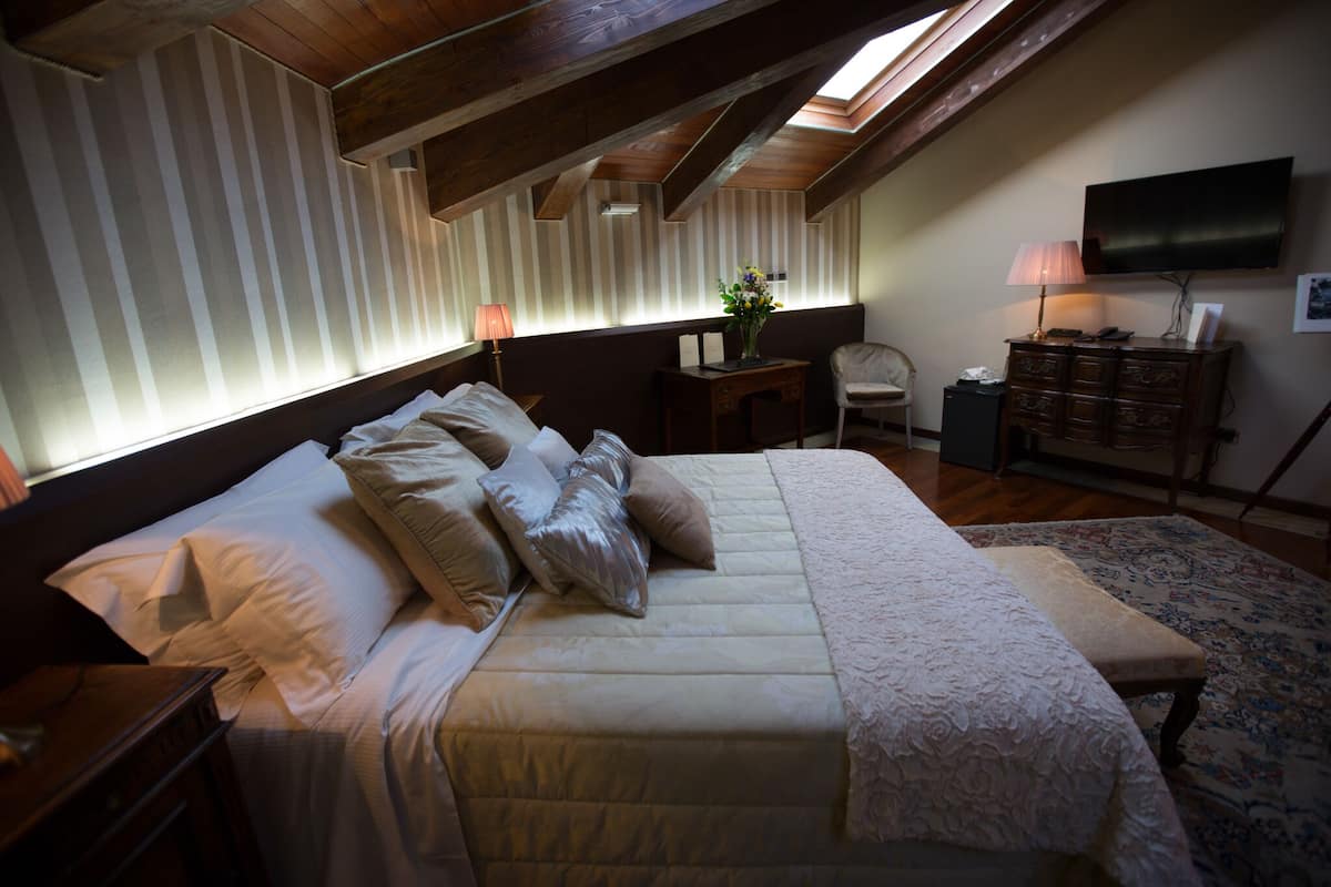 Un dormitorio con una cama grande, una mesita de noche, un aparador, una silla, un escritorio y un televisor en la pared.