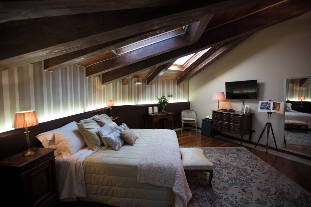 A bedroom with a large bed, a desk, a chair, a dresser, a television, and a skylight.