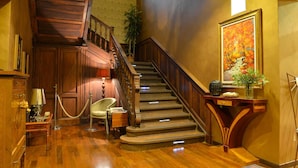 Una gran escalera con barandillas de madera y piso alfombrado que conduce a una zona de descanso con un jarrón de flores y un cuadro enmarcado.