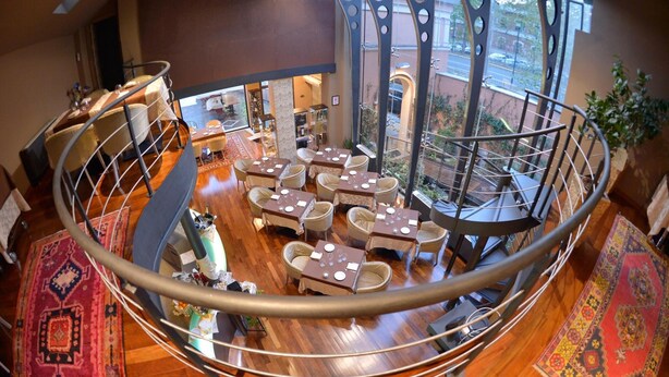 Un comedor amplio con mesas y sillas redondas, una escalera en espiral y vistas a la calle.