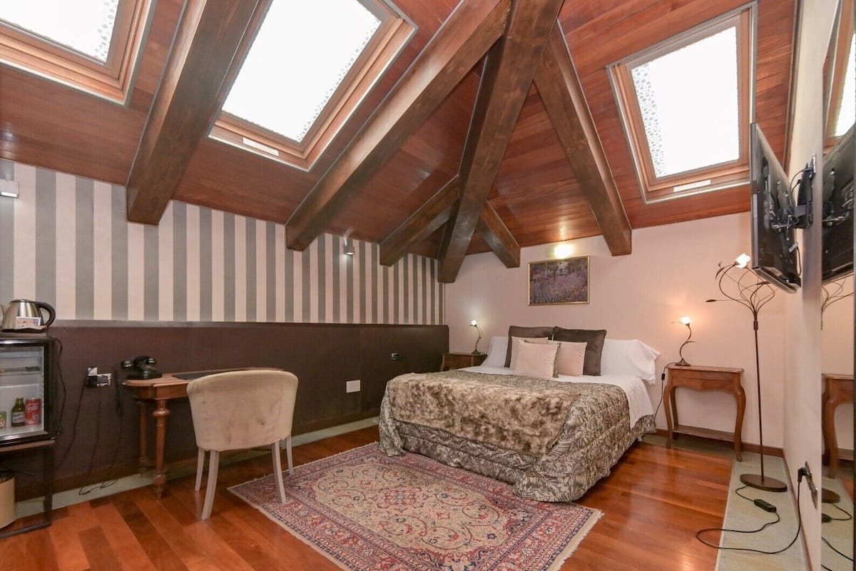 Un dormitorio con techo inclinado, una cama, una silla, un escritorio y un televisor.