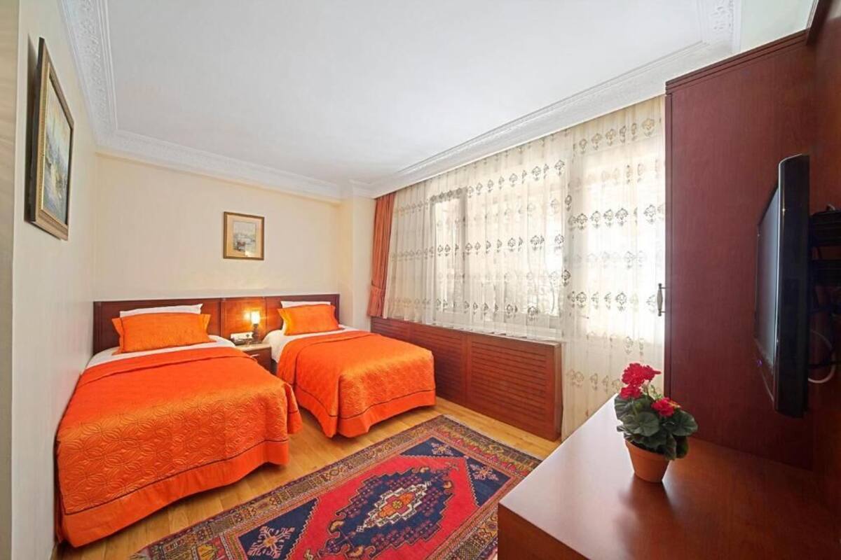 A hotel room with two beds, a wooden desk, a television, and a window with curtains.