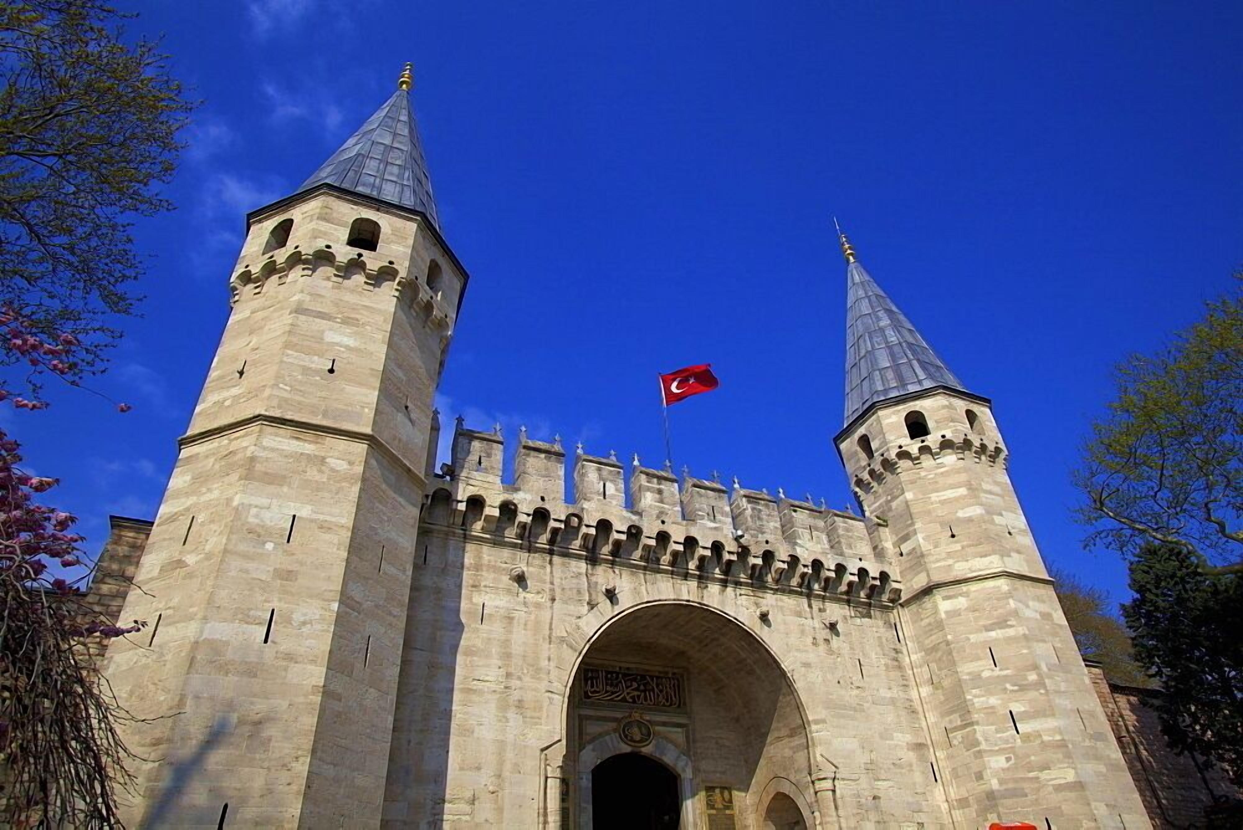 A historic stone gate with two towers, a flag, and an archway.