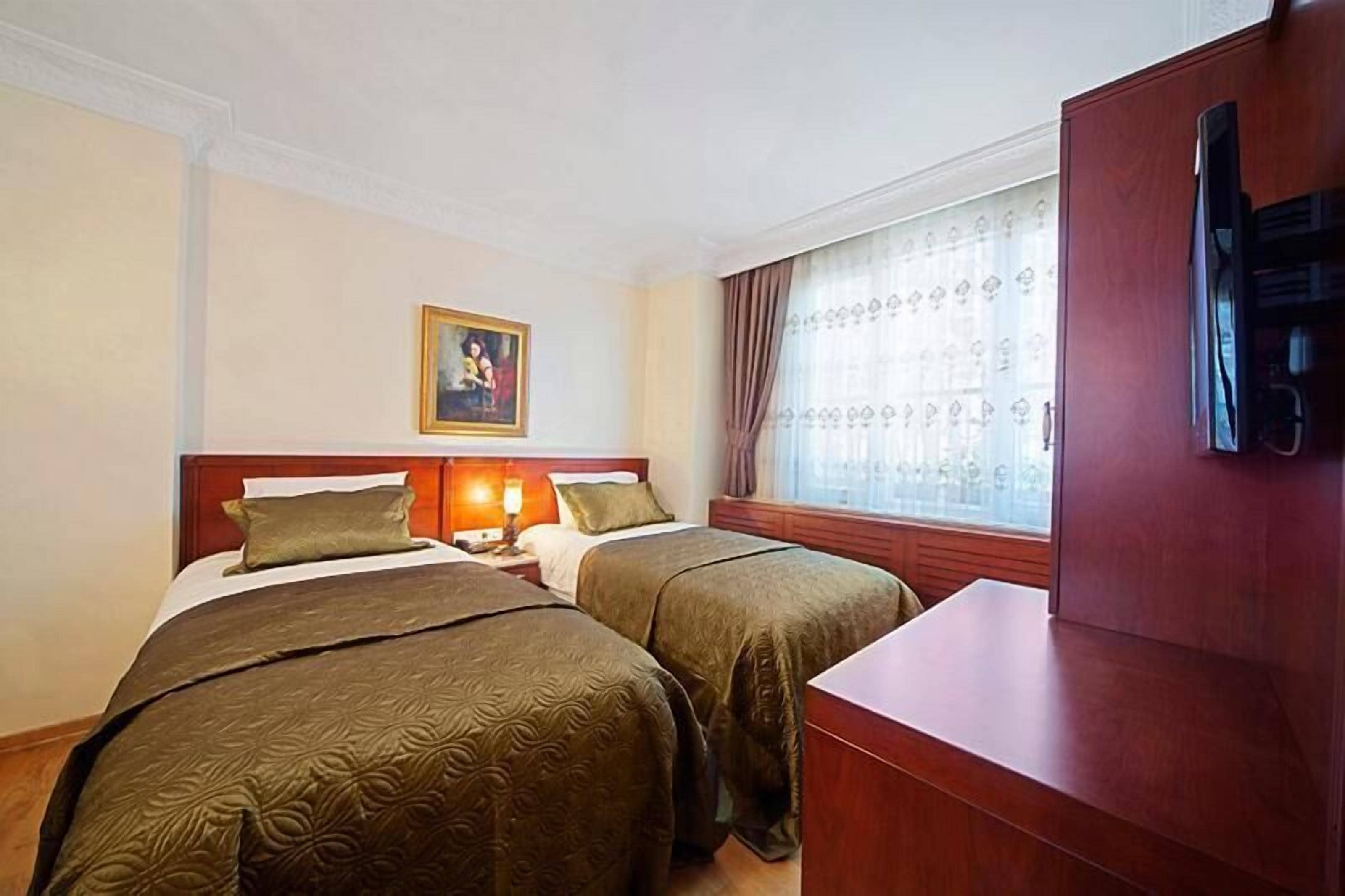 A hotel room with two beds, a desk, a television, and a window with curtains.