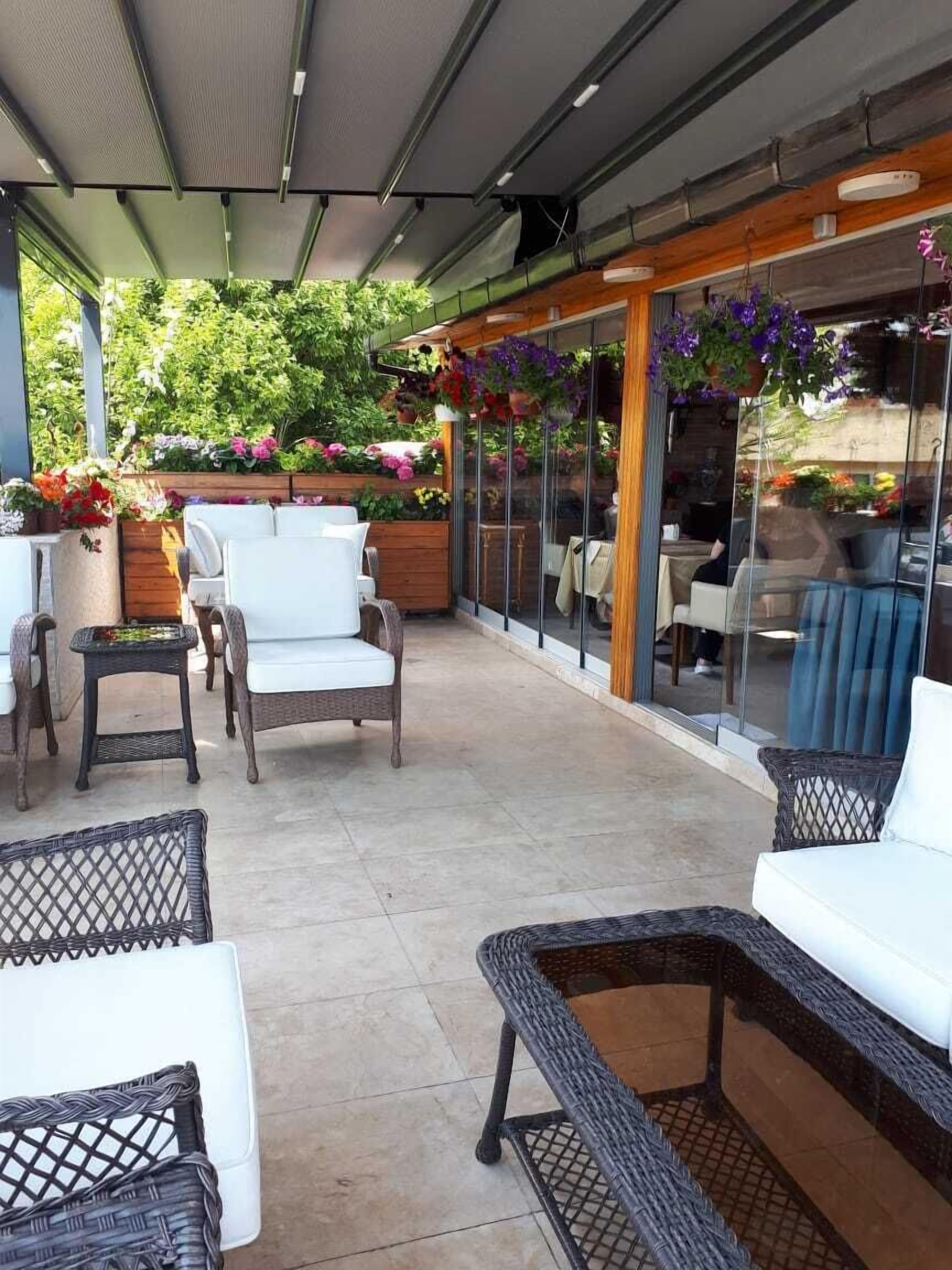 Un patio al aire libre con mobiliario de mimbre, un cerramiento de vidrio y una variedad de plantas en macetas.