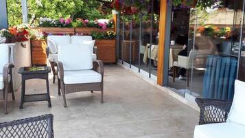 Un patio al aire libre con mobiliario de mimbre, un cerramiento de vidrio y una variedad de plantas en macetas.