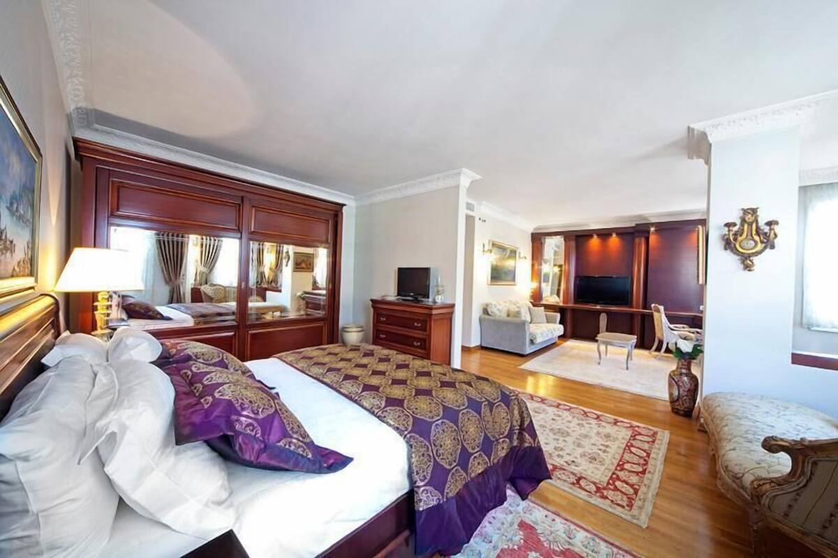 A spacious bedroom with a large bed, a sitting area with a sofa and chairs, and a TV.