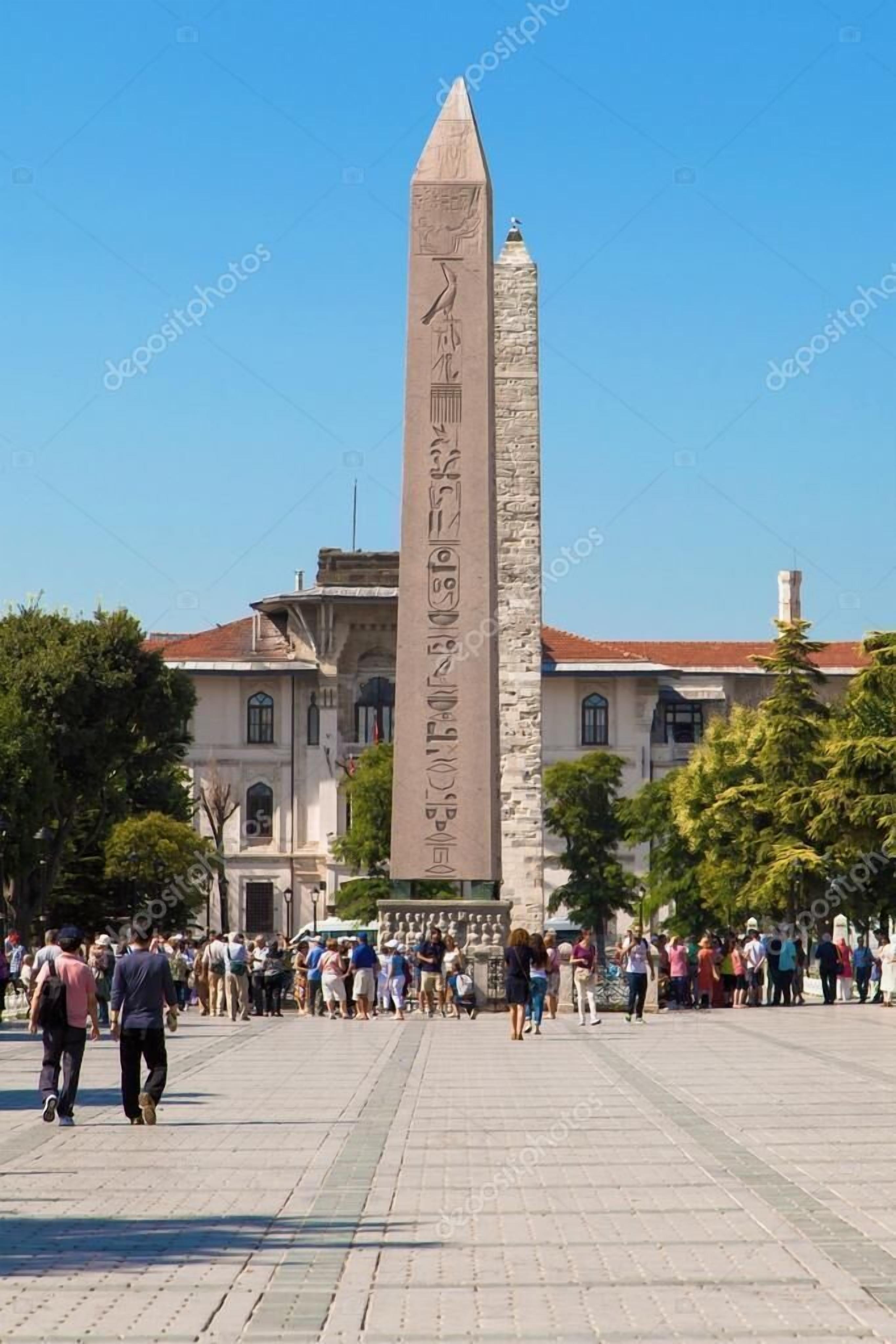 A large obelisk in a public square with a crowd of people around it.