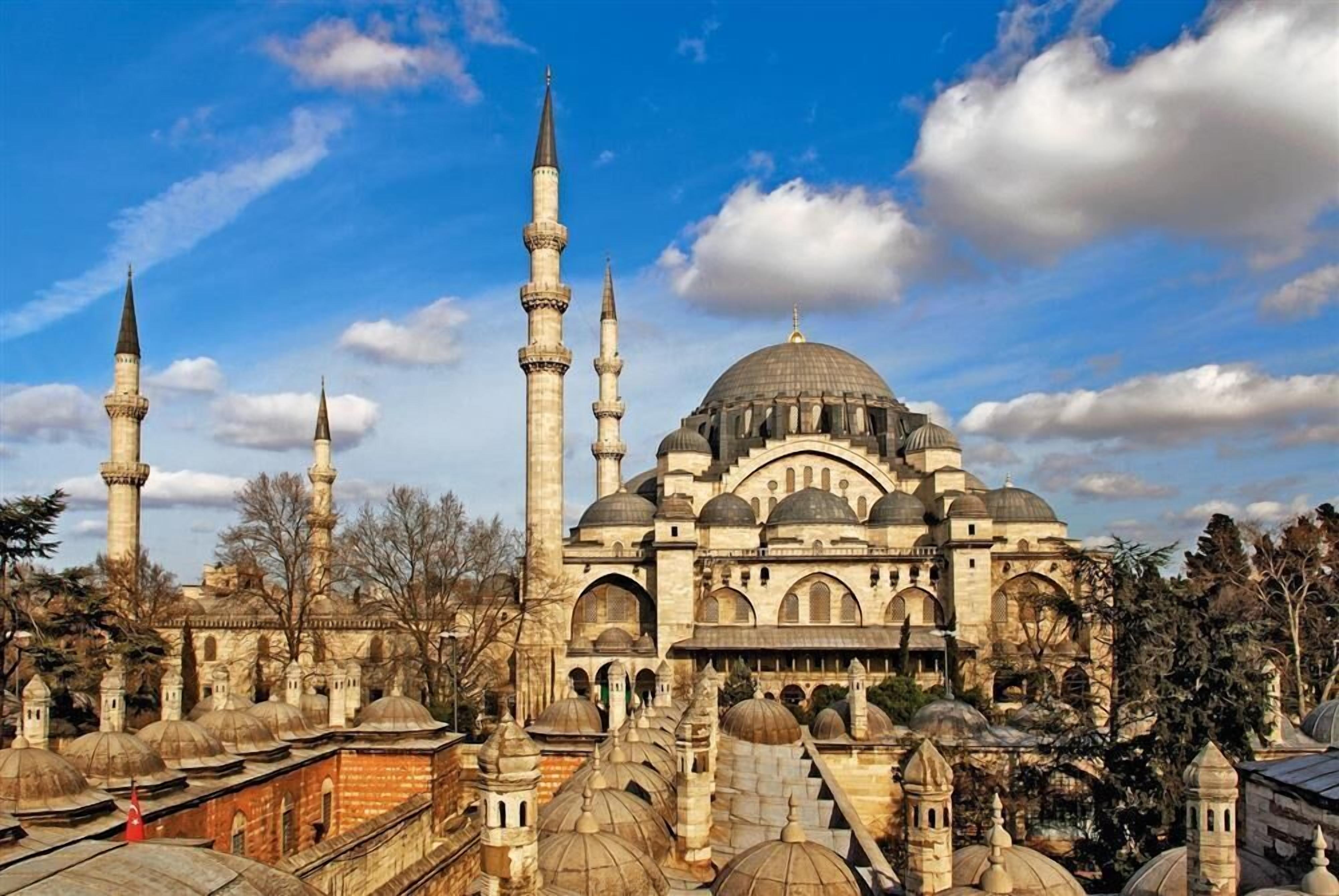 A historic mosque with multiple domes and minarets, surrounded by other buildings.