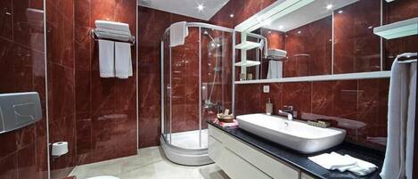 Um banheiro moderno com chuveiro em box de vidro, pia branca e um espelho grande.