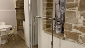 Una habitación con una mesa y sillas blancas, una estructura metálica, un muro de piedra y una puerta que da a otra habitación.