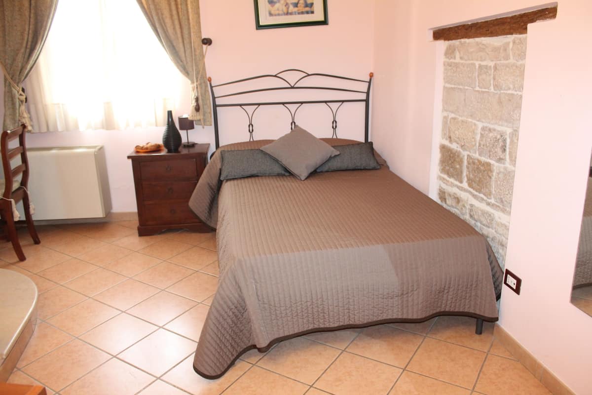 Un dormitorio con cama, mesita de noche, silla y ventana con cortinas.