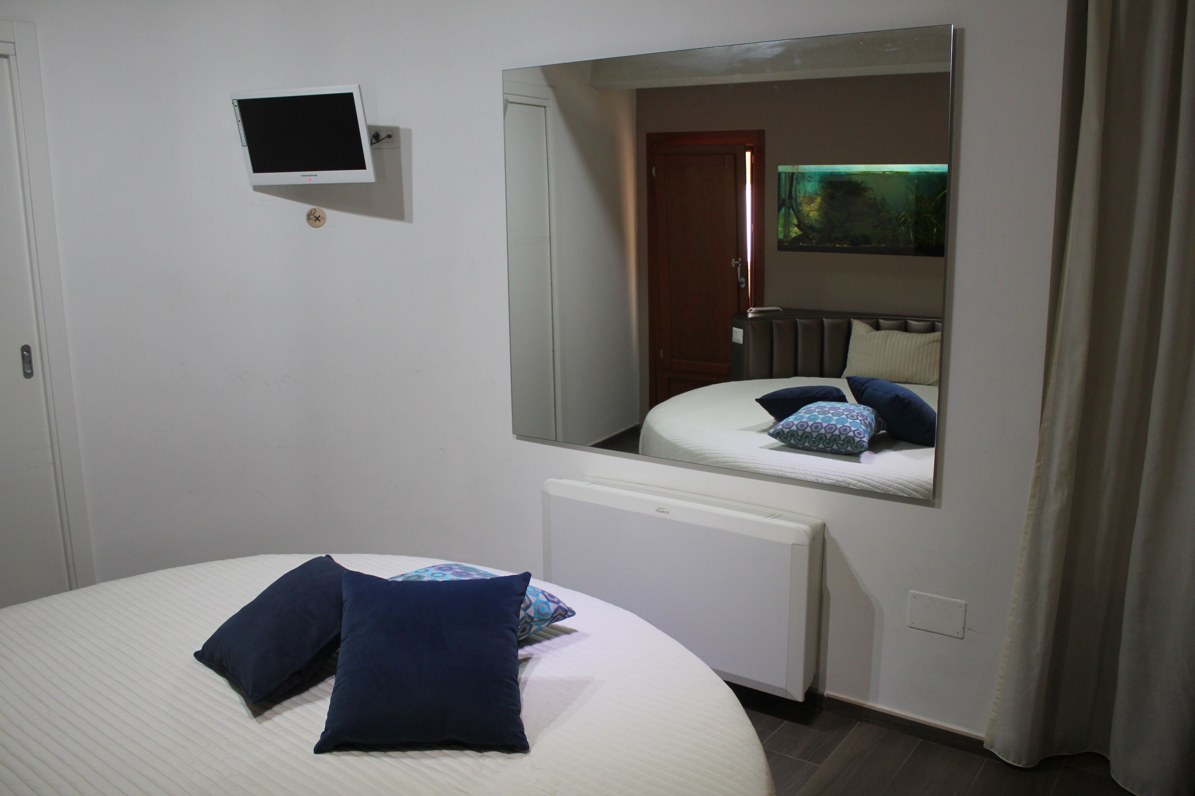 A hotel room with a bed, a small TV, a mirror, and a window with curtains.